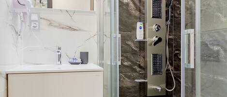 A modern bathroom with a glass-enclosed shower, a marble-tiled vanity, and a large mirror.