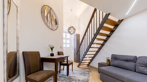 Un salon moderne avec un canapé gris, une table à manger en bois et des chaises, un escalier avec des marches en bois et un élément décoratif mural.