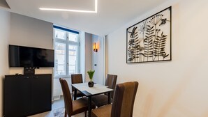 Un salon moderne doté d’un téléviseur à écran plat, d’une table à manger avec des chaises, d’une plante en pot et d’une grande œuvre d’art murale.
