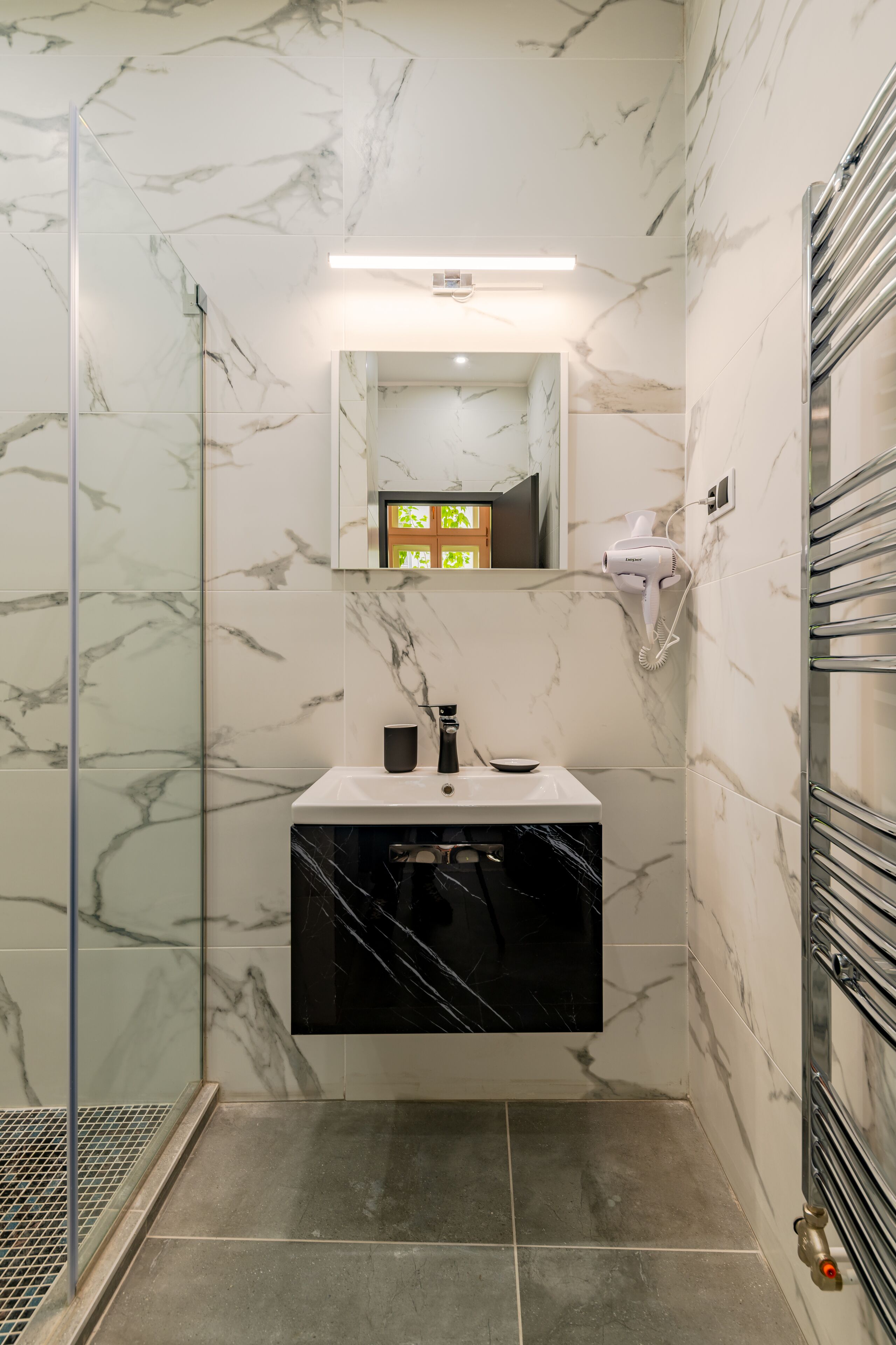 A bathroom with a glass shower enclosure, a sink with a black countertop, and a hairdryer mounted on the wall.