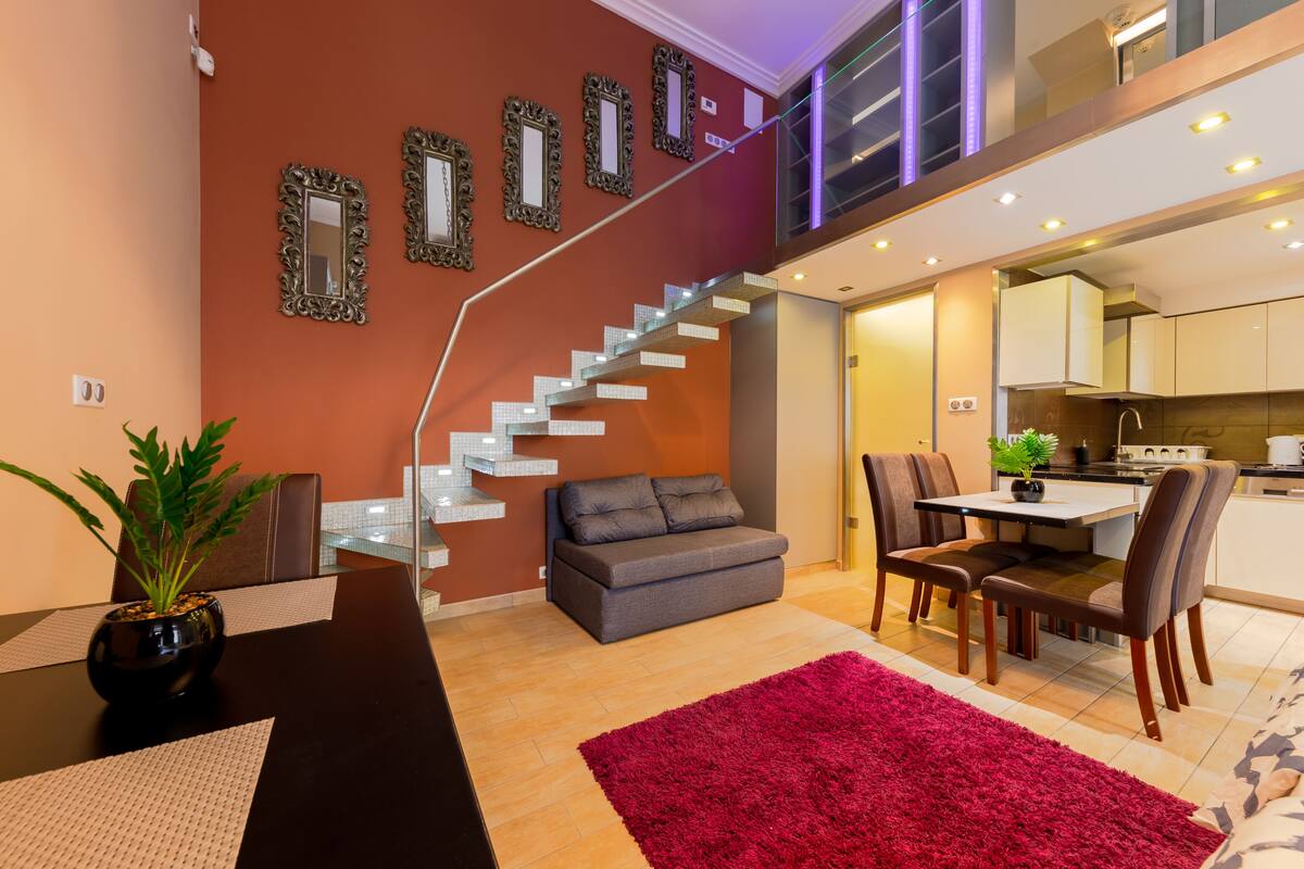 Una sala de estar moderna con una escalera, una zona de comedor y una cocina.