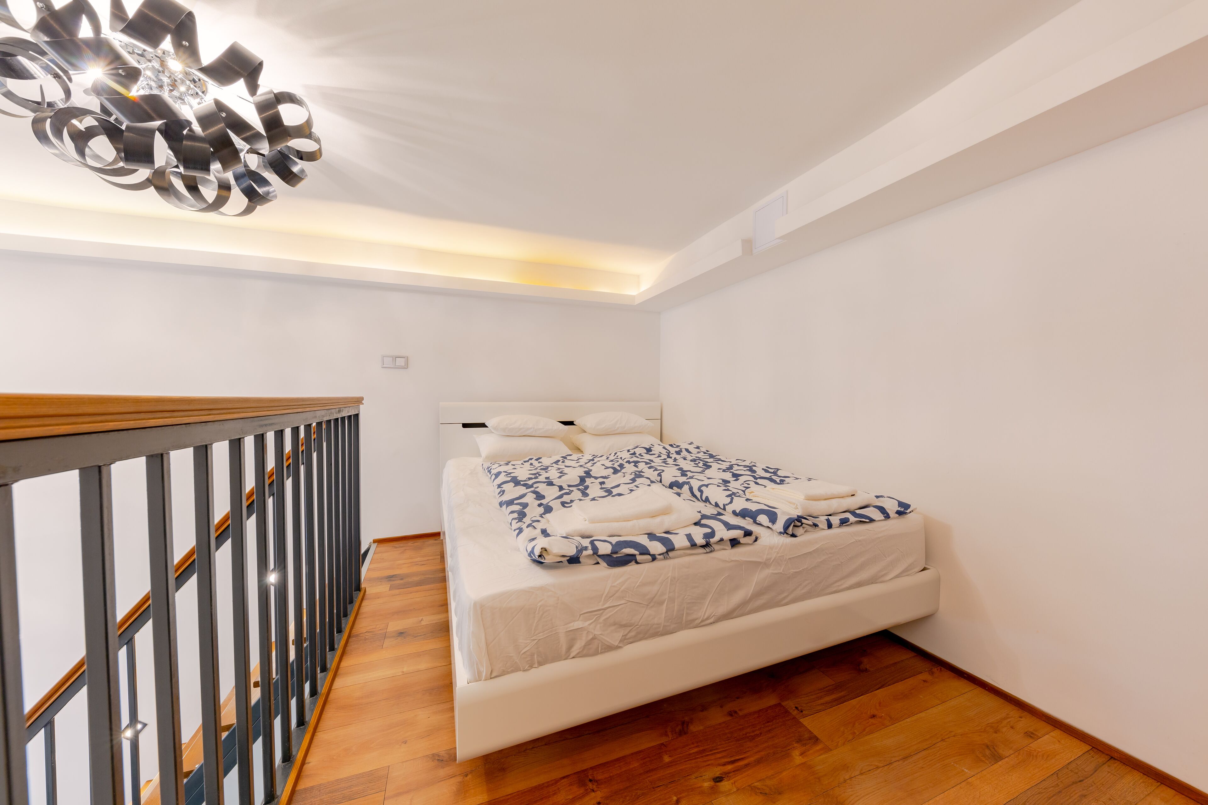 Un dormitorio con cama blanca, suelo de madera y una lámpara de araña moderna.