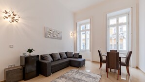 Un salon moderne comprenant un canapé d’angle, une table à manger avec des chaises, un petit réfrigérateur et un élément décoratif mural.