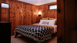 A wooden-paneled bedroom with a bed, a nightstand, and a wall-mounted lamp. - The Leeway - Two-Bedroom Suite (Mt Tremper)