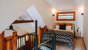 A bedroom with a sloped ceiling, a bed with patterned bedding, a small bedside table, and a window with wooden trim.