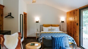 Un dormitorio con cama, una silla, una mesa, un ventilador de techo y una ventana.