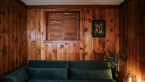 Ein Zimmer mit Holzwänden, einem grünen Sofa, einem Fenster mit Holzläden und einem gerahmten Bild an der Wand.