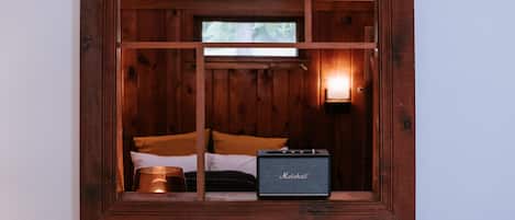 Une fenêtre à cadre en bois, avec un lit et un haut-parleur Marshall à l’intérieur.