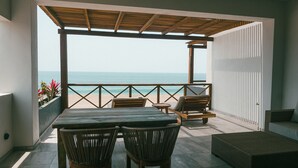 A covered outdoor seating area with a view of the sea, featuring a table and chairs, a sofa, and a wicker ottoman. - ROOM 7- Romantic 1 Bedroom Ocean Front Condo (El Rebase)