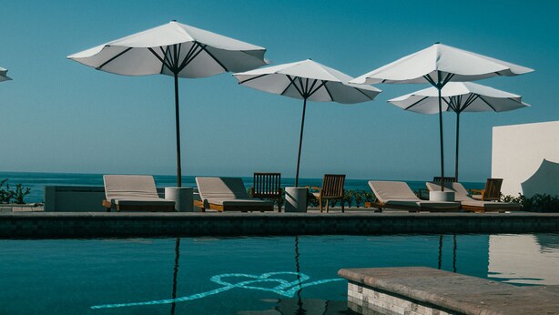 A poolside area with lounge chairs and umbrellas, a clear view of the ocean, and a heart-shaped design in the water. - ROOM 7- Romantic 1 Bedroom Ocean Front Condo (El Rebase)