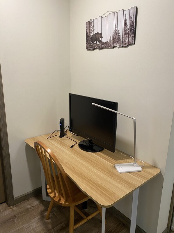 A wooden desk with a black monitor, a white desk lamp, and a smartphone charger.