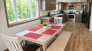 Una cocina con armarios de madera, una mesa de comedor con individuales rojos y una ventana con persianas.