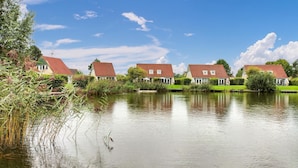 A row of houses with red roofs by a calm body of water, surrounded by greenery. - Lovely home in Vlagtwedde with kitchen (Vlagtwedde)