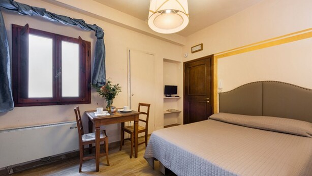 Una stanza con un letto, una scrivania con una sedia, una televisione e una finestra con tende.