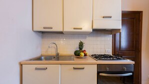 Una cucina compatta con lavandino, piano cottura e una ciotola di frutta sul ripiano.