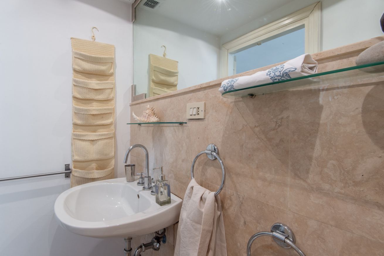 A bathroom with a sink, mirror, towel rack, and glass shelf.