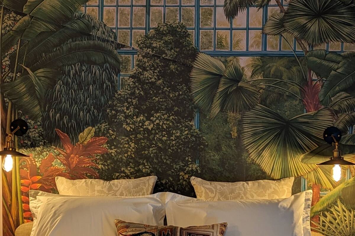 A bed with white linens and a tropical mural on the wall behind it.