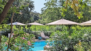A pool area with lounge chairs and umbrellas, surrounded by lush greenery and flowering plants. - La Galante  (Faugeres)