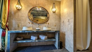 A bathroom with a marble vanity, two sinks, a large mirror, and wall-mounted sconces. - La Galante  (Faugeres)