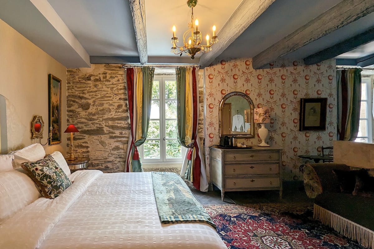 A bedroom with a large bed, a dresser, a mirror, and a chandelier.