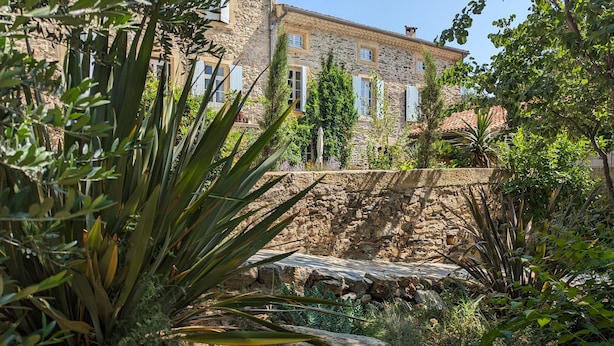 A stone building with a rustic facade, surrounded by lush greenery and a stone wall. - La Galante  (Faugeres)