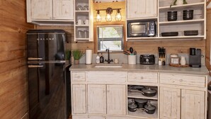 Eine kleine Küche mit einem Galanz-Kühlschrank, Holzschränken, einer Mikrowelle und verschiedenen Küchenutensilien.