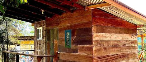 Una cabaña de madera rústica con un porche, una ventana pequeña y una puerta.