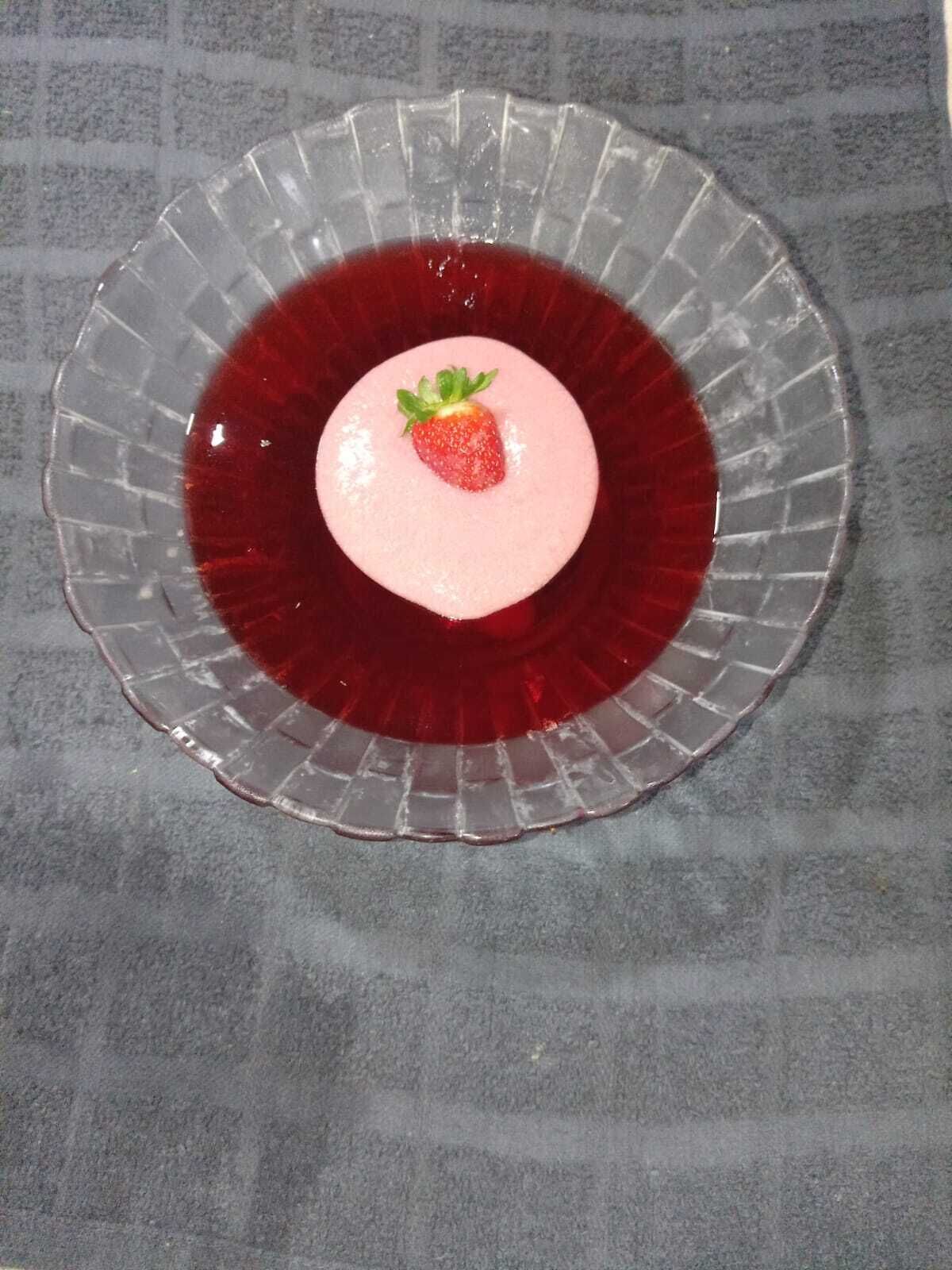 A dessert with a strawberry on top, placed on a glass plate.