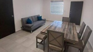 Ein geräumiges Zimmer mit Esstisch und Stühlen, einer Couch mit Kissen und einem Fenster mit Jalousien.