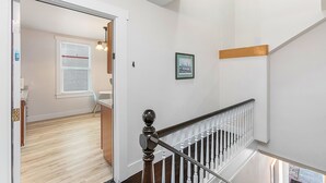 Eine Treppe mit weißer Geländer und Holzhandlauf, die zu einer oberen Etage führt. Ein gerahmtes Bild hängt an der Wand über der Treppe.