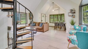 A spacious living area with a high ceiling, a spiral staircase, a sofa, a floral armchair, and a dining area with a table and chairs. - South Salem Vacation Rental w/ Furnished Deck! (South Salem)