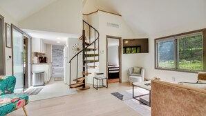 A spacious living area with a spiral staircase, a kitchen, and a large window offering a view of greenery. - South Salem Vacation Rental w/ Furnished Deck! (South Salem)