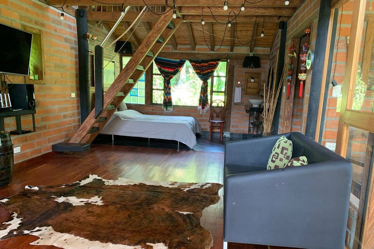 Una habitación rústica con una cama, un sofá, un tapiz de cuero de vaca y una pared de ladrillo.