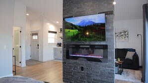 A modern living room with a flat-screen TV mounted on a stone wall, a fireplace, and a cozy seating area with a sofa and a coffee table. - Luxury Mountain Villa (Show Low)