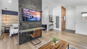 A modern living room with a stone accent wall, a mounted TV, a wooden coffee table, and a bed with a headboard. - Luxury Mountain Villa (Show Low)