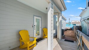Eine Holzterrasse mit zwei gelben Adirondack-Stühlen, einer Tür und Blick auf benachbarte Gebäude.