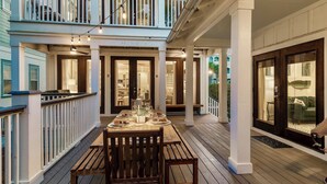 Une terrasse en bois avec une table à manger pour quatre personnes, un porche couvert et un bâtiment à deux étages doté d’un balcon.
