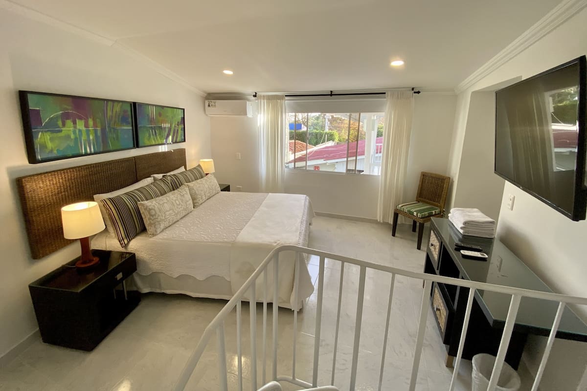 A hotel room with a bed, a desk, a chair, a TV, and artwork on the wall.