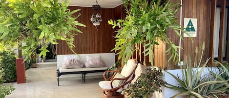 A modern indoor area with a wooden wall, a white sofa, a wicker chair, and several potted plants.