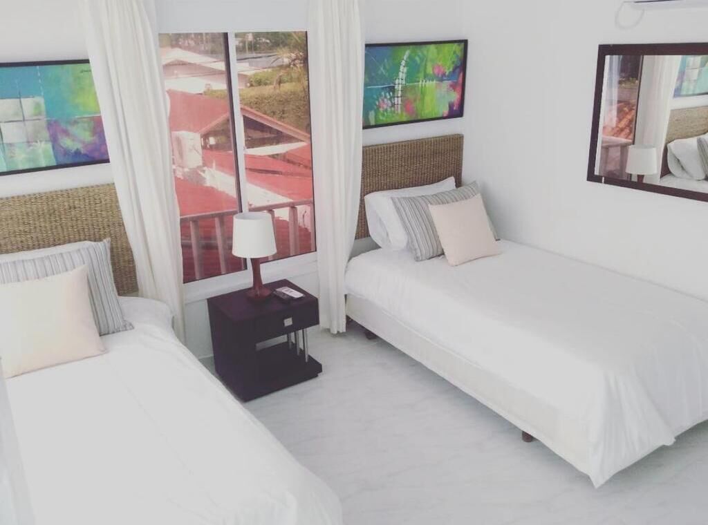 Habitación de hotel con dos camas, una mesita de noche, un ventanal con vistas y obras de arte en las paredes.