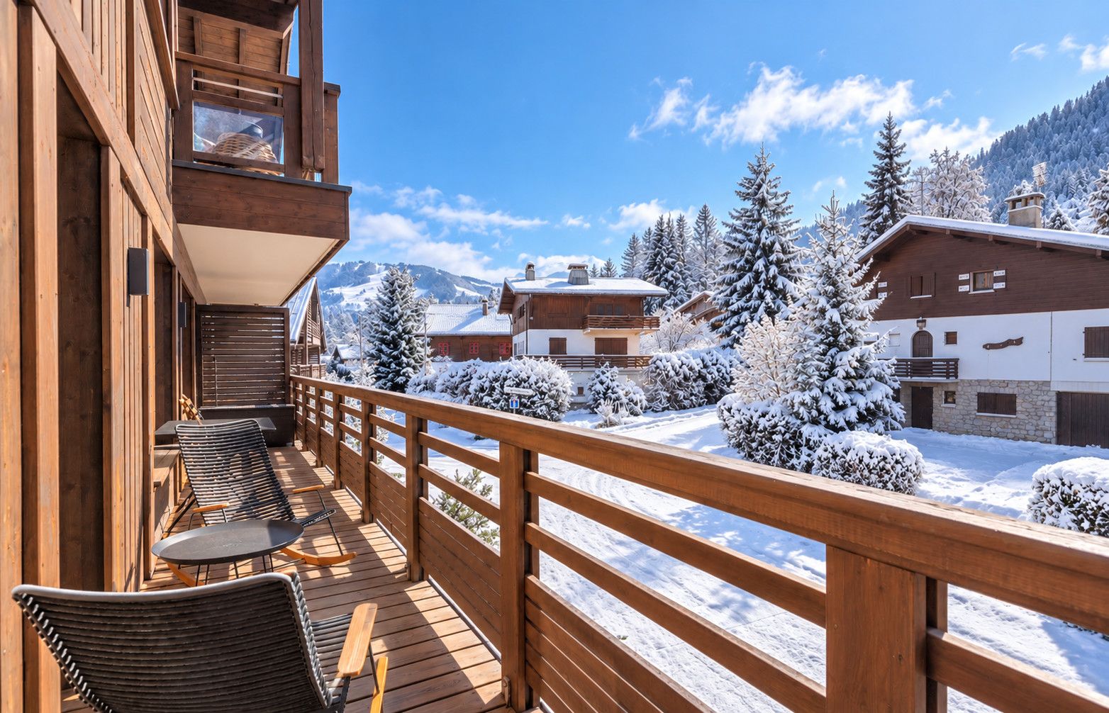 Une terrasse en bois avec des sièges extérieurs, offrant une vue sur un paysage enneigé parsemé de bâtiments et d’arbres.