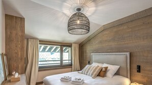 A modern bedroom with a large bed, a wooden ceiling, and a window with curtains.