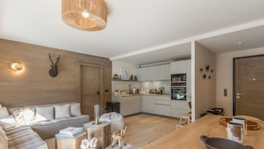 A modern living room with a wooden sofa, a dining table, and a kitchen in the background.
