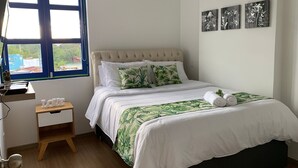 A bedroom with a bed, a small bedside table, a window with blinds, and three wall-mounted pictures. - Edificio San Jose Parque Guatape (Guatapé)