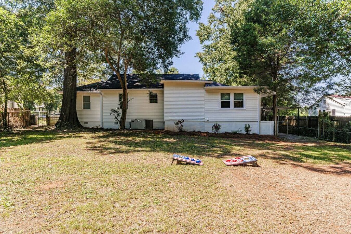 A single-story mobile home with a fenced yard, two small trees, and two lawn games.