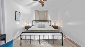 Ein Schlafzimmer mit einem Einzelbett, einem Deckenventilator, Nachttischlampen, einem gerahmten Bild an der Wand und einem Fenster mit Jalousien.
