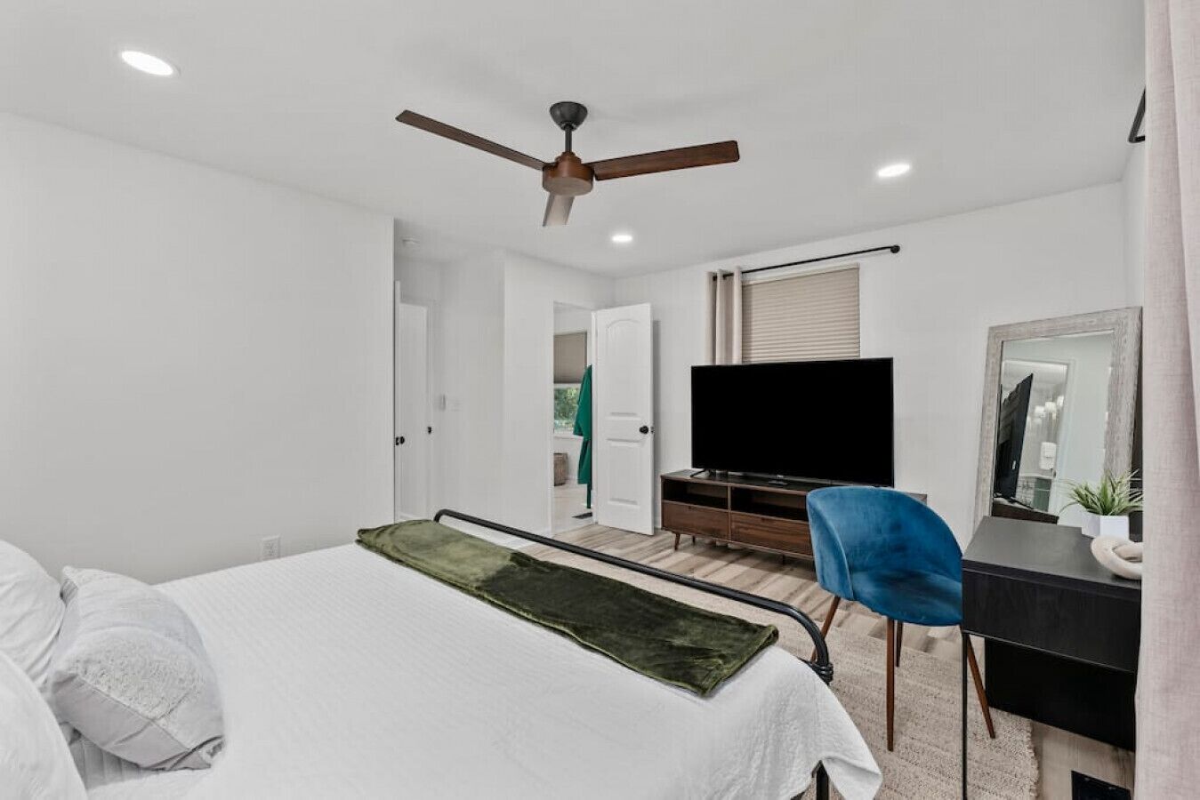 A modern bedroom with a bed, a desk, a television, and a ceiling fan.