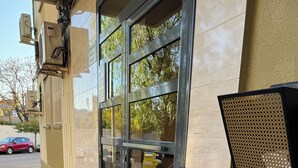 Entrada de un edificio con puerta de vidrio, barandilla de metal y piso texturizado.