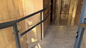 Un pasillo con suelo de mármol, barandillas de metal y una puerta de cristal.