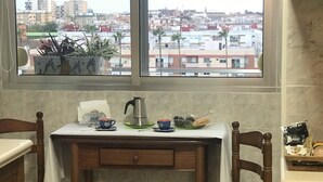 Una cocina pequeña con una mesa y dos sillas, una ventana con vista a la ciudad y un armario con un microondas.